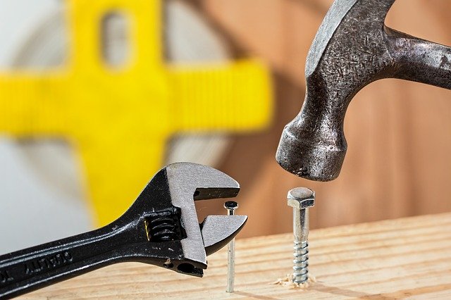 Symbolbild Robustheit - Hammer schlägt auf eine Schraube und ein Schraubenschlüssel bearbeitet einen Nagel